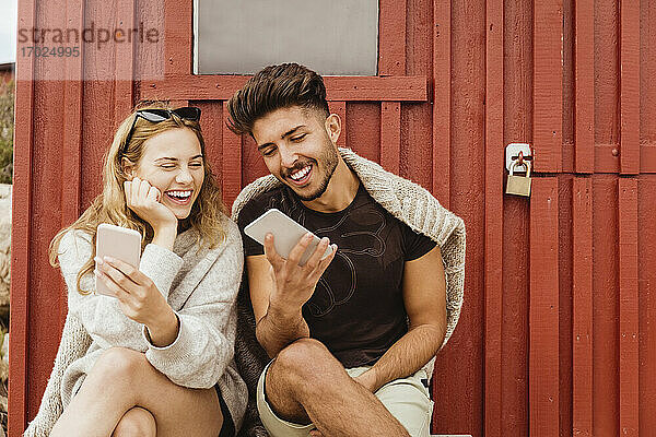 Freunde lachen bei der Verwendung von Mobiltelefon gegen Hütte