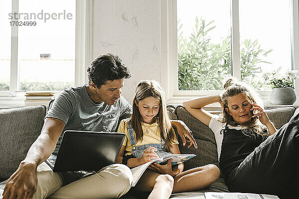 Tochter macht Hausaufgaben sitzend bei Mutter und Vater im Wohnzimmer