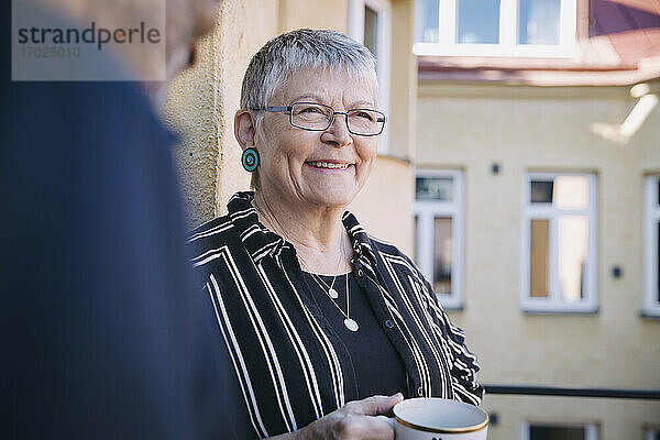Lächelnde Frau mit Kaffeetasse von Mann in Balkon