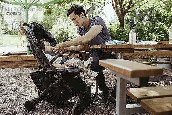 Vater füttert Baby Sohn beim Sitzen in Spielplatz