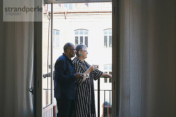 Senior Paar mit Kaffeetasse stehend auf dem Balkon zu Hause