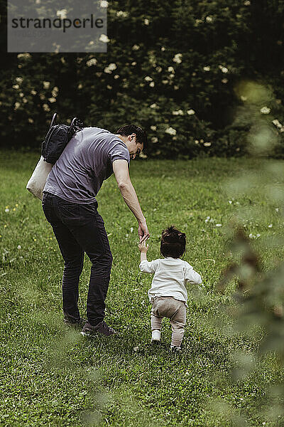 Vater hilft Baby-Sohn zu gehen auf Gras im Park