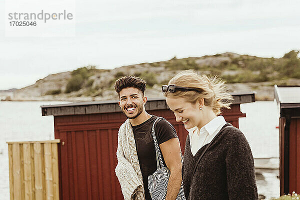 Lächelnder Mann  der seine Freundin anschaut  während er gegen den Himmel am Hafen steht