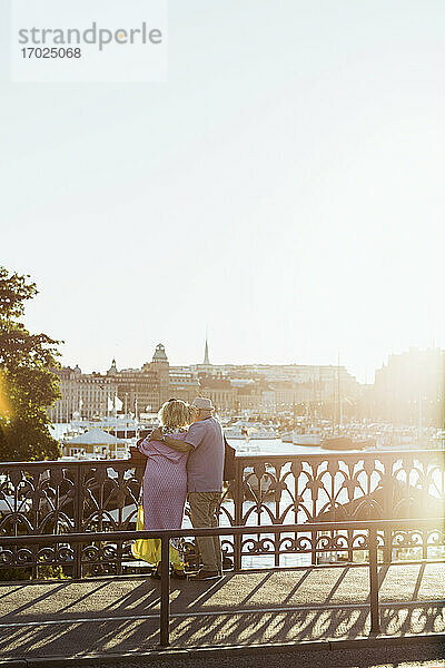 Rückansicht eines Paares  das auf einer Brücke stehend den Fluss betrachtet