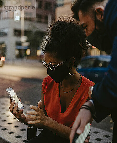 Weibliche Unternehmerin bei der Nutzung eines Smartphones mit einem männlichen Kollegen in einer Stadt während einer Pandemie