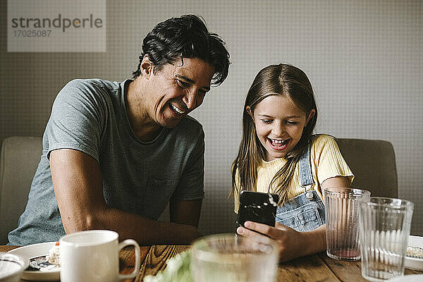 Lächelnder Vater und Tochter mit Mobiltelefon am Esstisch