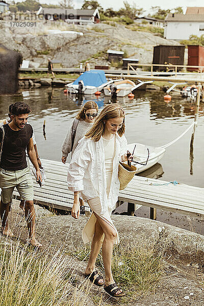 Glückliche Freunde zu Fuß auf Felsen am Meer am Hafen während Picknick