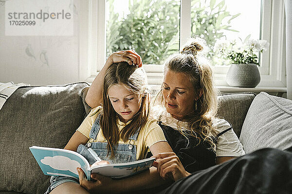 Tochter  die in ein Buch schreibt  während sie neben ihrer Mutter auf dem Sofa sitzt