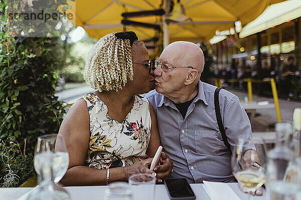 Senior Paar küssen sich gegenseitig  während am Bürgersteig Café sitzen
