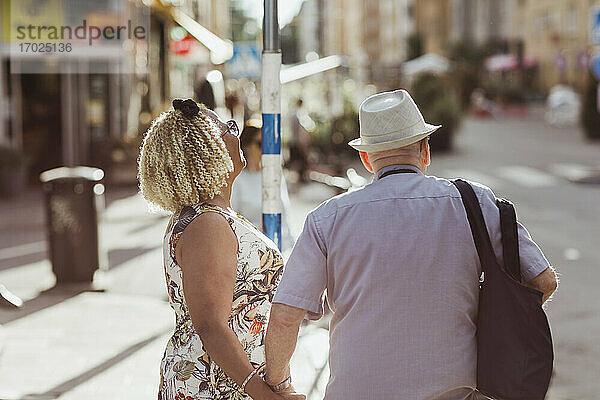 Senior Frau hält Hand auf Mann beim Spaziergang in der Stadt während des sonnigen Tages