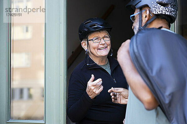 Lächelndes Seniorenpaar mit Fahrradhelm an der Eingangstür zu Hause