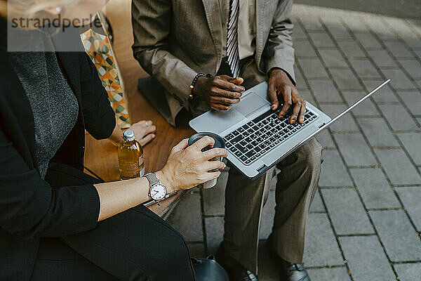 Ausgeschnittenes Bild von männlichen und weiblichen Kollegen  die über einen Laptop diskutieren  während sie auf einer Bank sitzen