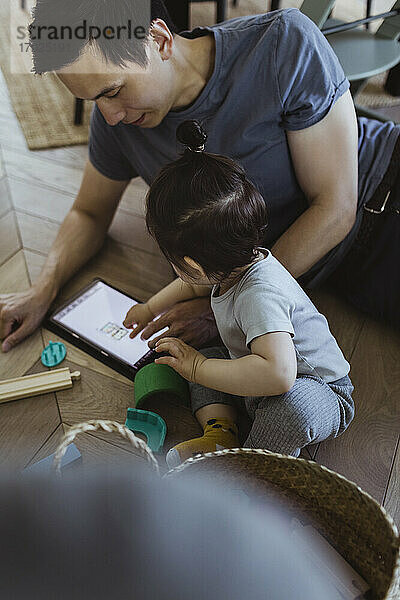 Vater mit digitaler Tablette sitzt mit Baby Sohn zu Hause