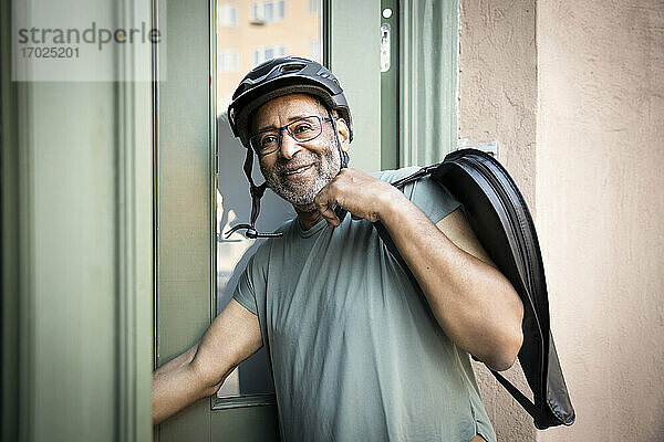 Lächelnder älterer Mann mit Tasche am Eingang vor dem Haus