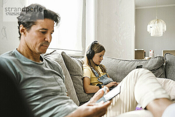 Der Vater benutzt ein Smartphone  während die Tochter mit dem Laptop im Wohnzimmer e-Learning betreibt