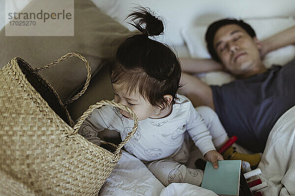Männliches Kleinkind späht im Korb  während der Vater zu Hause auf dem Bett schläft