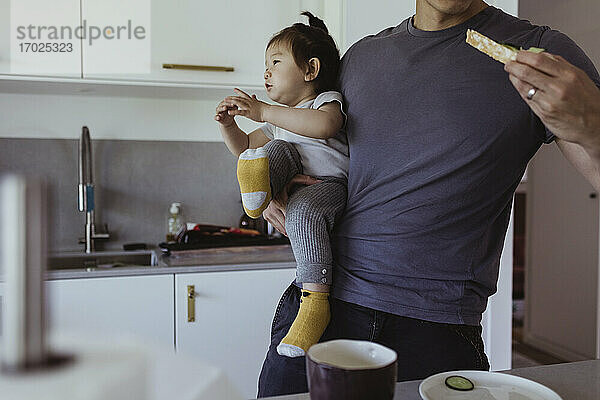 Mittelteil des Vaters  der Essen isst  während er seinen Sohn in der Küche trägt