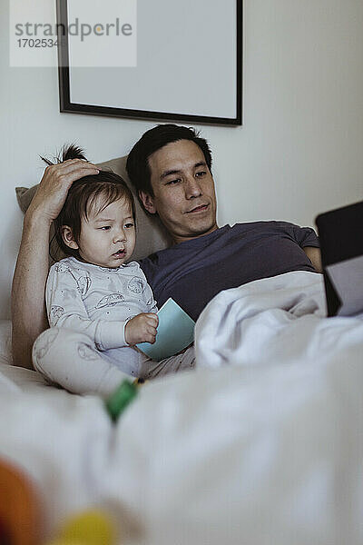 Vater benutzt digitales Tablet von männlichem Kleinkind im Schlafzimmer