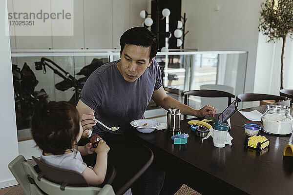 Vater füttert männliches Kleinkind über Tisch zu Hause