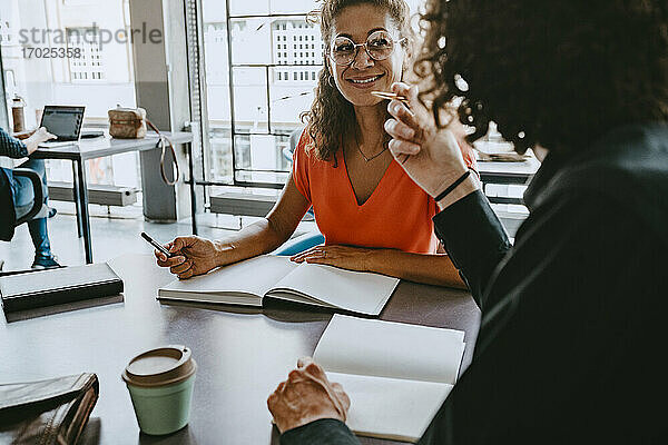 Lächelnde Geschäftsfrau  die mit einem männlichen Kollegen im Coworking-Büro diskutiert