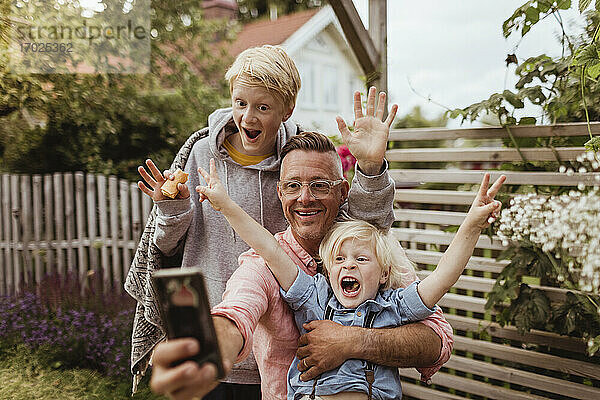 Fröhlicher Vater nimmt Selfie mit Söhnen auf Smartphone im Vorgarten am Abend