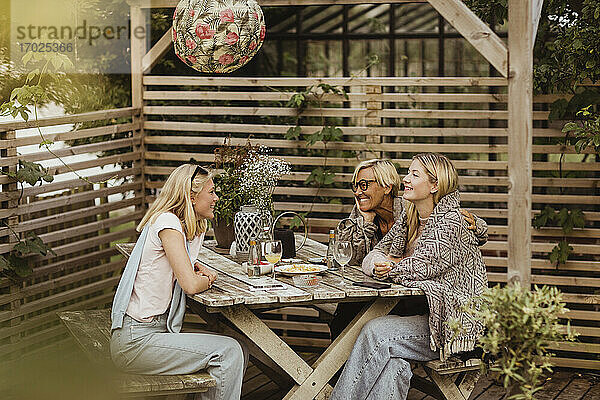 Lächelnde Freundinnen verbringen Zeit mit Großmutter am Tisch im Vorgarten