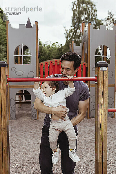 Männliches Kleinkind mit Vater auf dem Spielplatz an der Affenstange hängend