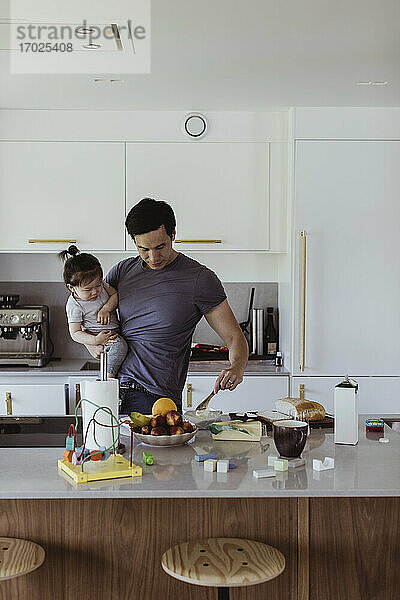 Vater trägt Baby Sohn während der Zubereitung von Speisen in der Küche