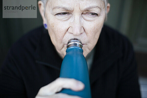 Ältere Frau trinkt Wasser vor dem Haus