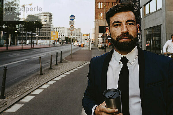 Porträt eines Geschäftsmannes mit isoliertem Getränkebehälter auf dem Fußweg stehend