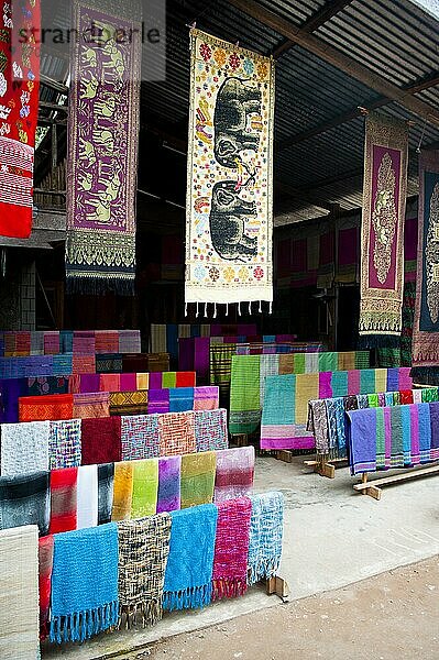 Schals zum Verkauf auf einem Markt außerhalb von Luang Prabang  Laos. Eine Konstante in Südostasien ist die Abhängigkeit von Kunst und Kunsthandwerk  und Luang Prabang ist da keine Ausnahme. Gleich außerhalb des Stadtzentrums finden Sie alle Arten von Kunsthandwerk  einschließlich Weberei und Holzschnitzerei.