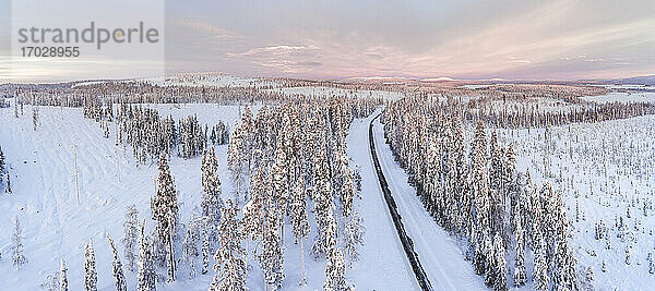 Eisige  schneebedeckte Winterstraße am Polarkreis bei Sonnenuntergang in Lappland  Finnland