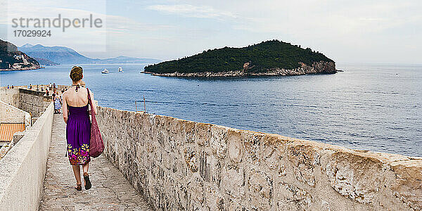 Panoramafoto eines Touristen  der auf der Stadtmauer von Dubrovnik spazieren geht  Altstadt von Dubrovnik  Kroatien. Dies ist ein Panoramafoto von einem Touristen  der auf der Stadtmauer von Dubrovnik spazieren geht  mit der Insel Lokrum im Hintergrund. Für Touristen sind die Stadtmauern von Dubrovnik eines der beliebtesten Ausflugsziele in Dubrovnik  da sie einen unglaublichen Panoramablick über die gesamte Altstadt von Dubrovnik und die Adriaküste  einschließlich der Insel Lokrum  bieten.