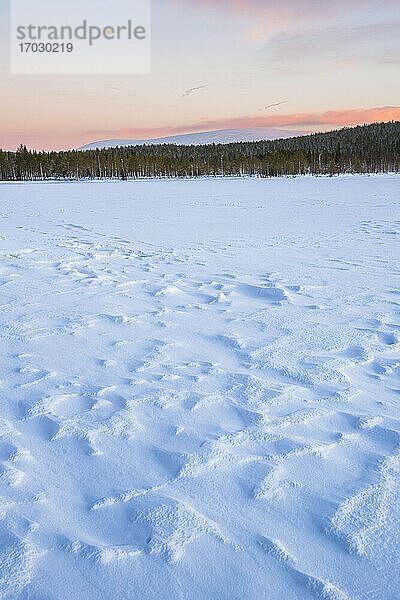 Gefrorener schneebedeckter See in der Winterlandschaft in Lappland bei Sonnenuntergang innerhalb des Polarkreises in Finnland