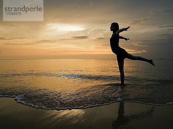 Eine junge Frau am Strand bei Sonnenuntergang macht Yoga-Übungen