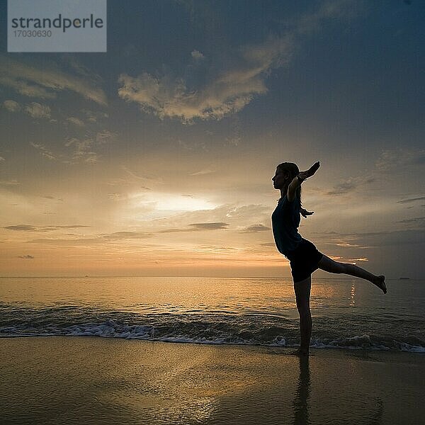 Eine junge Frau am Strand bei Sonnenuntergang macht Yoga-Übungen