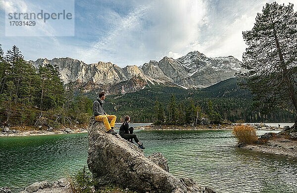 Junge Frau und junger Mann sitzen auf einem Felsen am Ufer  Blick in die Ferne  Eibsee vor Zugspitzmassiv mit Zugspitze  Wettersteingebirge  bei Grainau  Oberbayern  Bayern  Deutschland  Europa