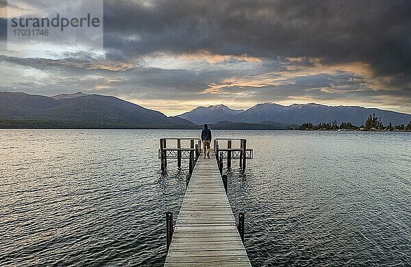 Juger Mann auf Steg am See  Lake Te Anau bei Sonnenuntergang  Te Anau  Südinsel  Neuseeland  Ozeanien