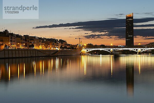 Blick über den Fluss Rio Guadalquivir mit beleuchteter Brücke Puente de Triana  hinten Hochhaus Torre Sevilla  Sonnenuntergang  blaue Stunde  Sevilla  Andalusien  Spanien  Europa