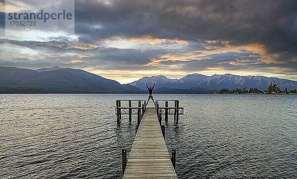 Juger Mann macht einen Luftsprung  Steg am See  Lake Te Anau bei Sonnenuntergang  Te Anau  Südinsel  Neuseeland  Ozeanien