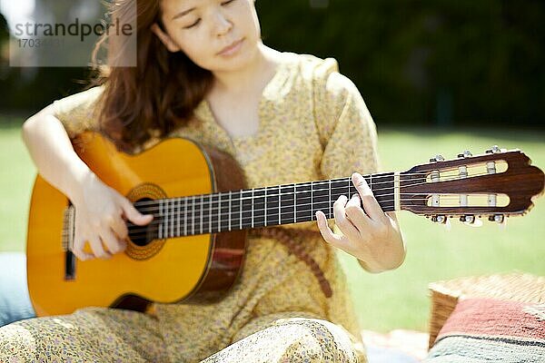Japanische Frau spielt Gitarre im Garten