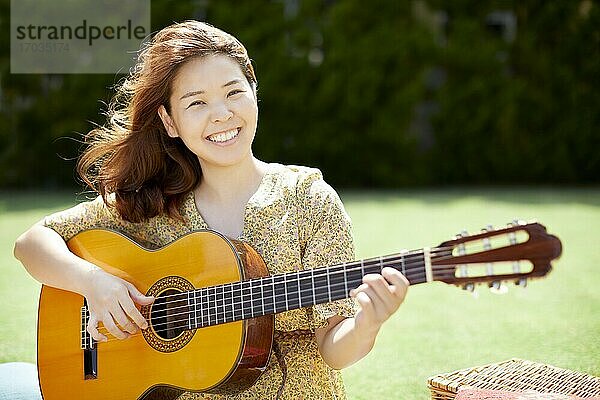 Japanische Frau spielt Gitarre im Garten