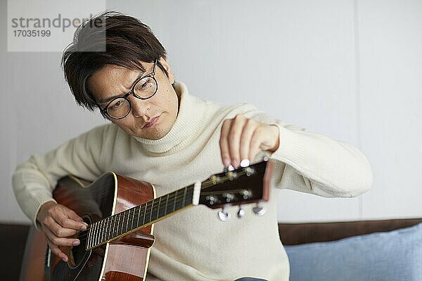 Japanischer Mann spielt Gitarre zu Hause