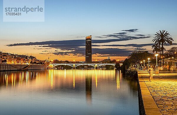 Blick über den Fluss Rio Guadalquivir mit beleuchteter Brücke Puente de Triana und Uferpromenade  hinten Hochhaus Torre Sevilla  Sonnenuntergang  blaue Stunde  Sevilla  Andalusien  Spanien  Europa