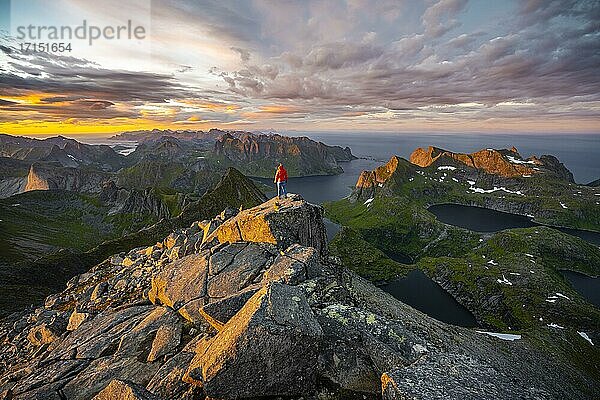 Wanderin steht am Gipfel  Sonnenuntergang mit dramatischen Wolken  Ausblick vom Gipfel des Hermannsdalstinden  Fjorde  Seen und Berge  Moskenesøya  Lofoten  Nordland  Norwegen  Europa