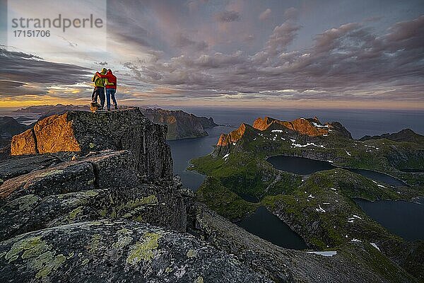 Zwei Wanderer am Gipfel  Sonnenuntergang mit dramatischen Wolken  Ausblick vom Gipfel des Hermannsdalstinden  Fjorde  Seen und Berge  Moskenesøya  Lofoten  Nordland  Norwegen  Europa