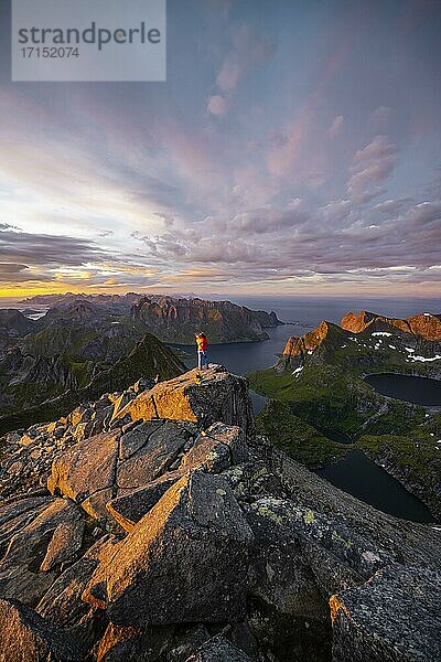 Wanderin steht am Gipfel  Sonnenuntergang mit dramatischen Wolken  Ausblick vom Gipfel des Hermannsdalstinden  Fjorde  Seen und Berge  Moskenesøya  Lofoten  Nordland  Norwegen  Europa