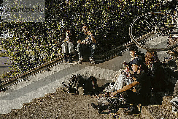 Freunde mit Essen und Trinken beim Sitzen auf Stufen im Park