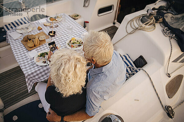 Hoher Winkel Ansicht der älteren Paar nehmen Selfie auf Handy in Segelboot während des Sonnenuntergangs