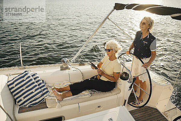 Ältere Frau segelt Boot  während Freundin mit digitalem Tablet
